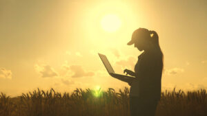 An image of a woman holding a computer in front of a field for our article answering the question, "Can I get an agriculture degree online?"